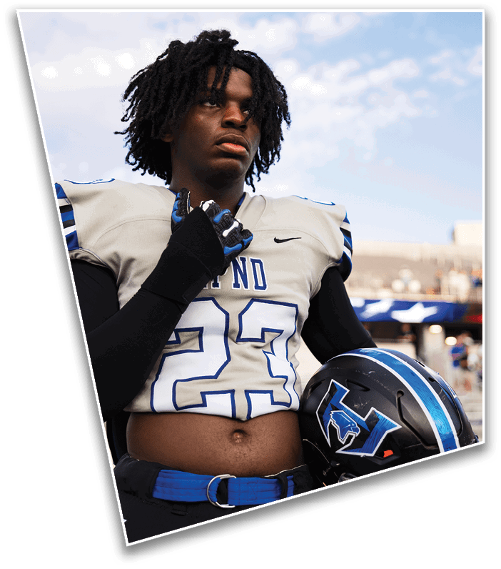 A person with dreadlocks wearing a football uniform and glove looks thoughtfully into the distance against a partly cloudy sky. Description generated by AI