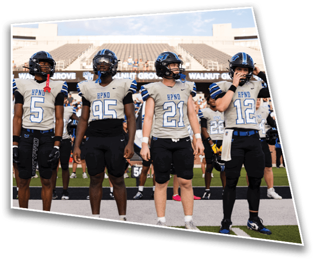 Four people wearing football uniforms stand side by side on a field with a stadium in the background. Description generated by AI
