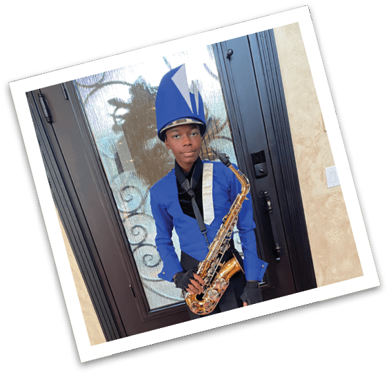 A person dressed in a blue and black marching band uniform with a tall blue hat is holding a saxophone while standing indoors in front of a glass door. Description generated by AI