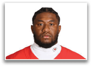 Person wearing a red sports jersey and a white undershirt with a logo, looking directly at the camera against a plain white background. Description generated by AI