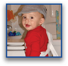 A child wearing a red long-sleeve shirt and denim pants is standing near a bathtub with a white cloth draped over their shoulder. Description generated by AI