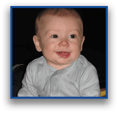 A smiling child wearing a light-colored shirt is looking slightly to the side against a dark background. Description generated by AI