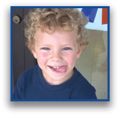 A child with curly hair wearing a dark shirt is smiling and playfully sticking out their tongue. Description generated by AI