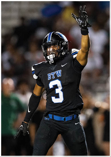 A person wearing a black football uniform with “BTW" on the chest and a helmet is raising one arm, appearing to celebrate or signal during a game. Description generated by AI