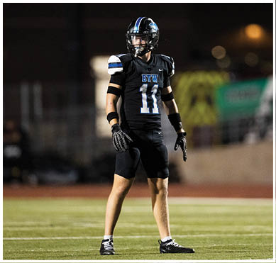 A person wearing a black football uniform with the number 11 and the letters BTW stands on a field at night, appearing ready for action. Description generated by AI