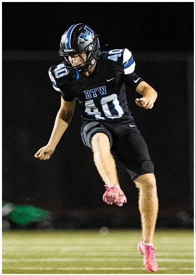 A person wearing a black football uniform with the number 40 is kicking a football on a field at night. Description generated by AI