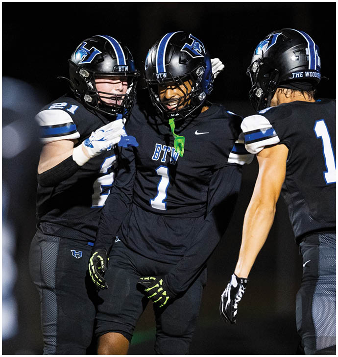 Three people in black football uniforms with helmets are celebrating on a field at night. Description generated by AI