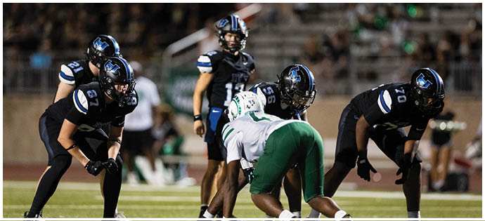 Five people in football uniforms are positioned on a field, appearing ready for a play during a game. Description generated by AI