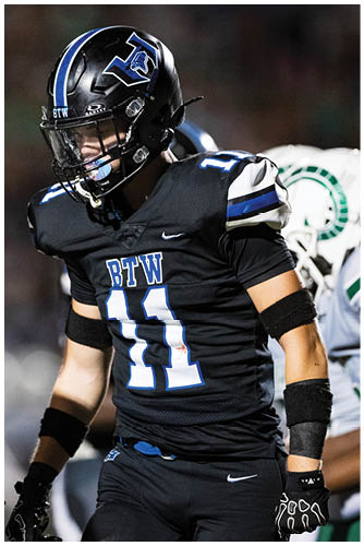 Two people in black football uniforms and helmets are interacting on a field during a game. Description generated by AI