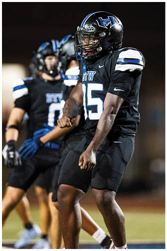 A person wearing a black football uniform with the number 15 is standing on a field with other players in similar uniforms in the background. Description generated by AI