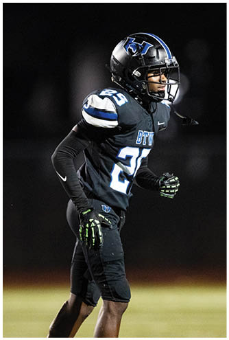A person wearing a black football uniform with the number 25 and a helmet is standing on a field at night. Description generated by AI