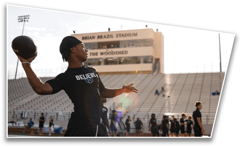 A person wearing a black shirt and headband is preparing to throw a football on a sports field with empty bleachers and a stadium building in the background. Description generated by AI