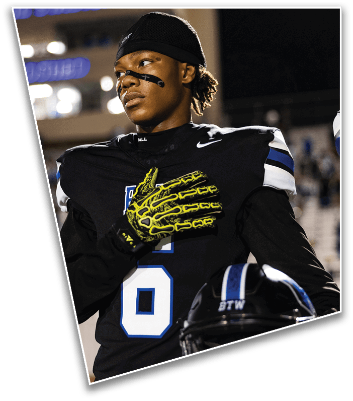 A person wearing a black sports uniform with a headband and yellow gloves is looking to the side with a focused expression, standing under bright lights. Description generated by AI