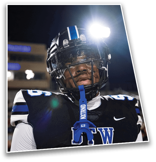A person wearing a football helmet with a blue stripe is illuminated by a bright light against a dark night sky. Description generated by AI