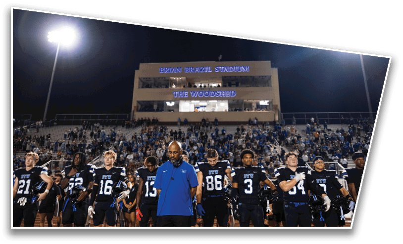 A group of people in football uniforms and a coach in a blue shirt stand on a field in front of a stadium crowd at night. Description generated by AI