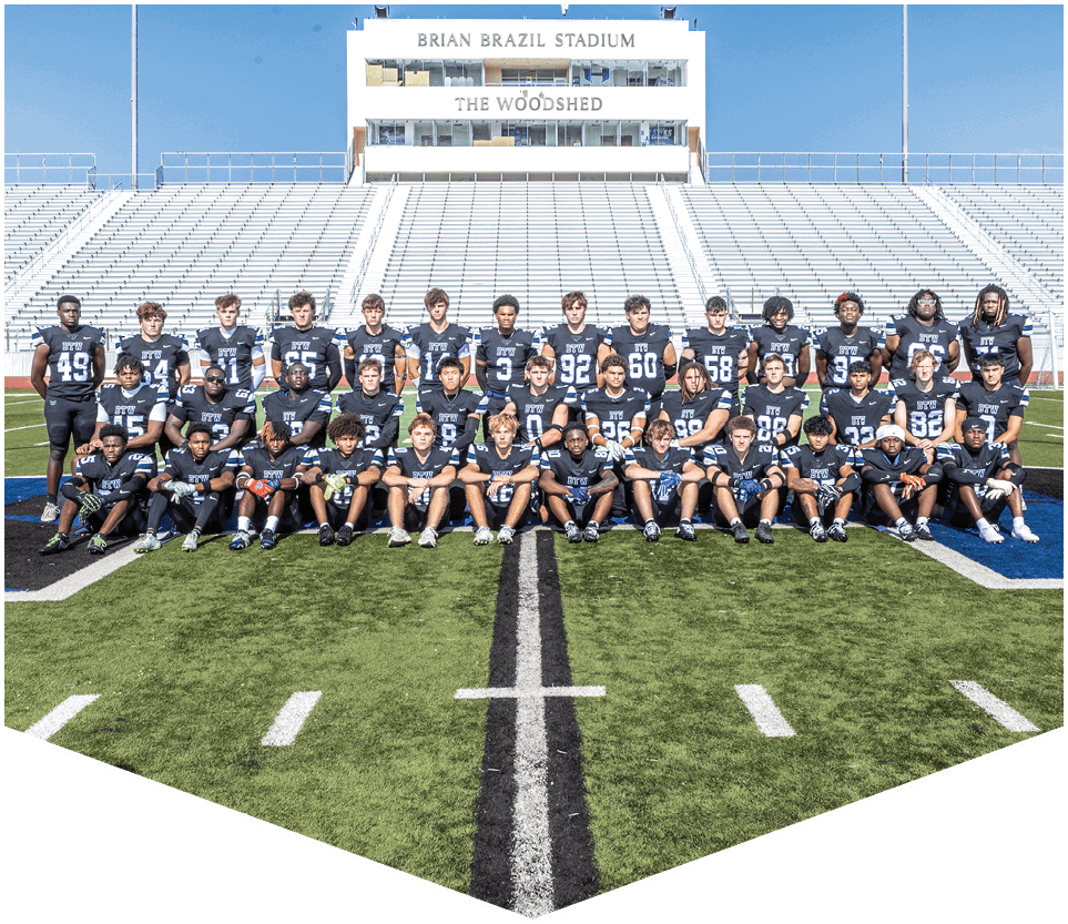 A group of nine people wearing black football uniforms with “HAWKS" written on the front stand side by side on a football field under a clear blue sky. Description generated by AI