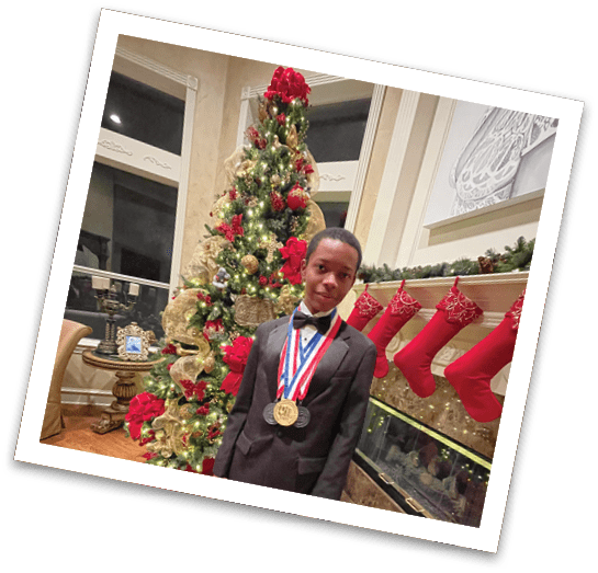 A person dressed in a black suit with a bow tie stands indoors near a decorated Christmas tree and fireplace wearing multiple medals around their neck. Description generated by AI