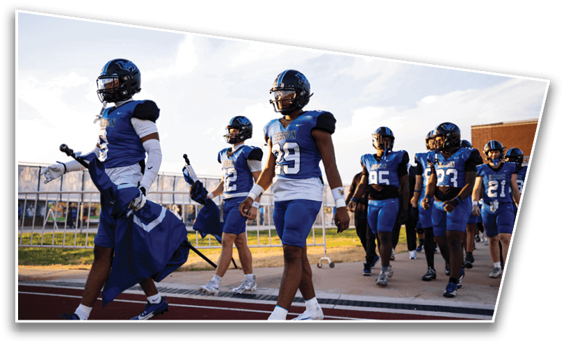 A group of people wearing blue and white football uniforms and helmets are walking together on a track near a field. Description generated by AI