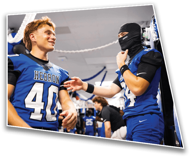 Two people in blue football uniforms are interacting in a decorated indoor space, with one person wearing a balaclava and the other smiling. Description generated by AI