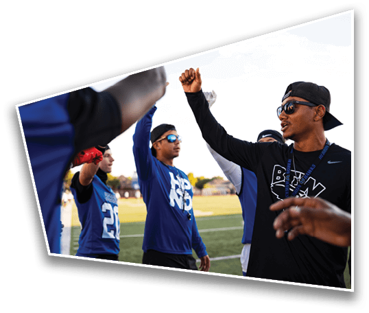 A group of people wearing sports jerseys and sunglasses are raising their fists together on a field, appearing to celebrate or motivate each other. Description generated by AI