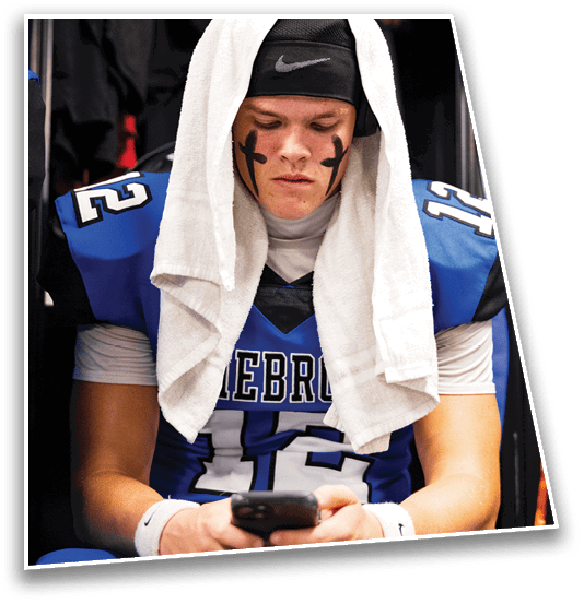 A person wearing a sports uniform with a towel draped over their head and black face paint in the shape of crosses on their cheeks looks down with a serious expression. Description generated by AI
