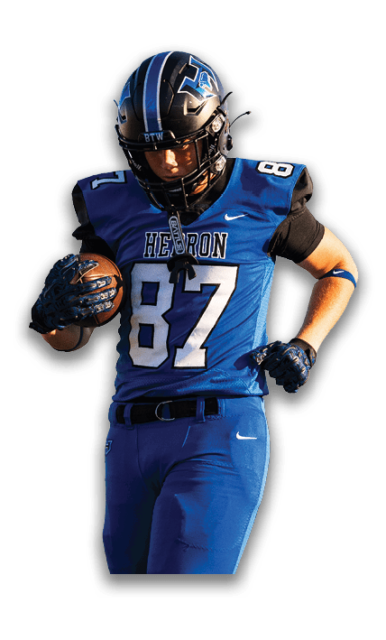 A person wearing a blue football uniform with the number 87 and a helmet is holding a football while running. Description generated by AI