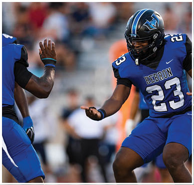 Two football players in blue and black uniforms with helmets are engaging in a celebratory gesture on the field. Description generated by AI