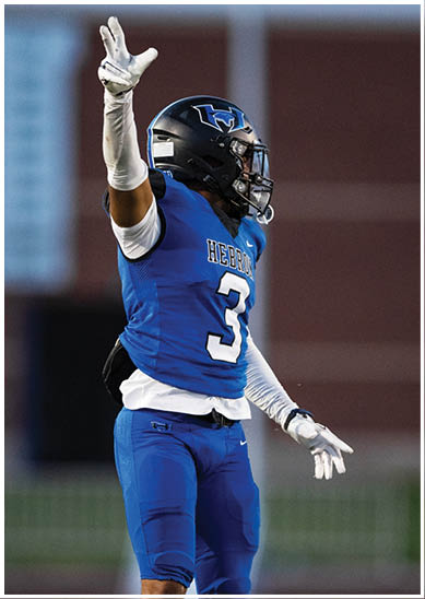 A person wearing a blue football jersey with the word “HEBRON" and the number 3 raises one arm while wearing a black helmet with a blue and white logo. Description generated by AI