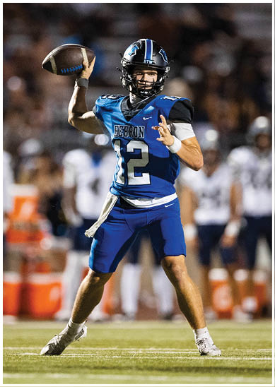 A person wearing a blue and black football uniform with the number 12 is preparing to throw a football during a game. Description generated by AI