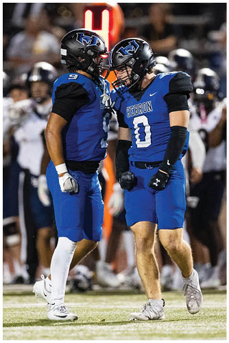 A person wearing a blue football uniform with the word “HEBRON" and the number zero on the jersey is standing on a field during a game. Description generated by AI