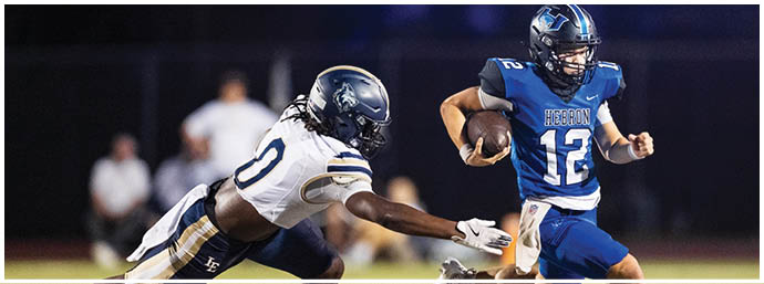 Two people in football uniforms are on a field with one person running with the ball while the other lunges forward attempting to tackle. Description generated by AI