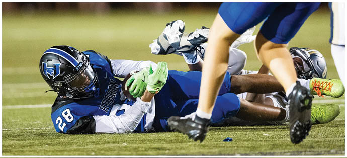 Two people in football uniforms are on the ground during a game, with one holding a football tightly while another player stands nearby. Description generated by AI