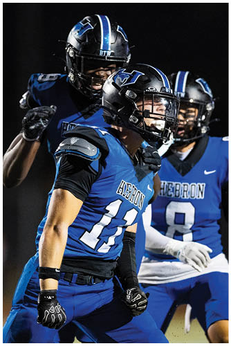 Three people in blue and black football uniforms with helmets appear to be celebrating or preparing during a nighttime game. Description generated by AI