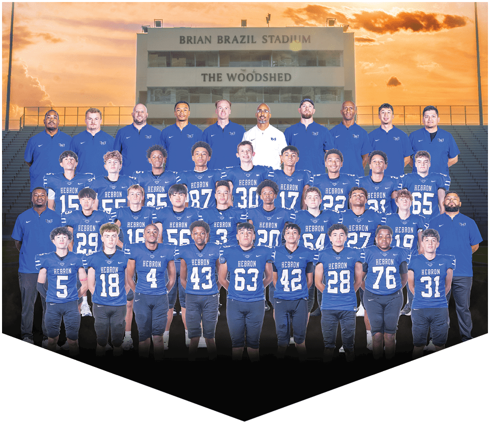 A group of adults and youths wearing matching sports uniforms and polo shirts pose together on a football field with a stadium building labeled Brian Brazil Stadium and The Woodshed in the background during sunset. Description generated by AI