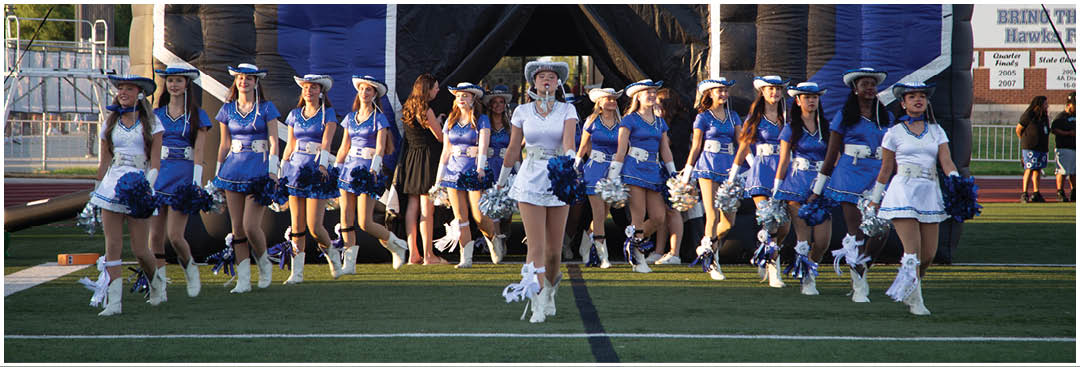 A group of people dressed in blue and white cheerleading uniforms with pom-poms are walking together on a sports field. Description generated by AI