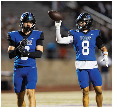 A person wearing a blue football uniform with the number 8 and the word Hebron is holding a football in a throwing position on a field. Description generated by AI