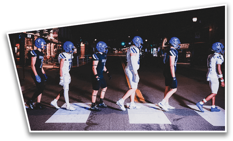 People wearing black American Canyon football uniforms and helmets are standing on a football field at night. Description generated by AI