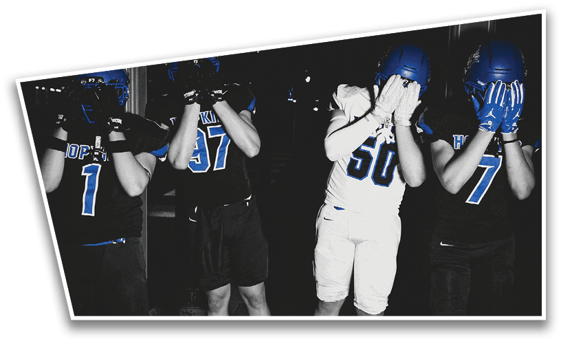 People wearing black American Canyon football uniforms and helmets are standing on a football field at night. Description generated by AI