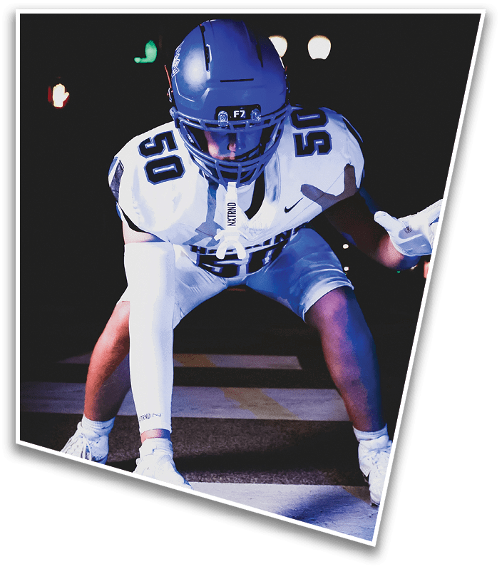 A person wearing a dark football uniform and helmet with “American Canyon" on the jersey is kneeling on one knee on a field at night. Description generated by AI