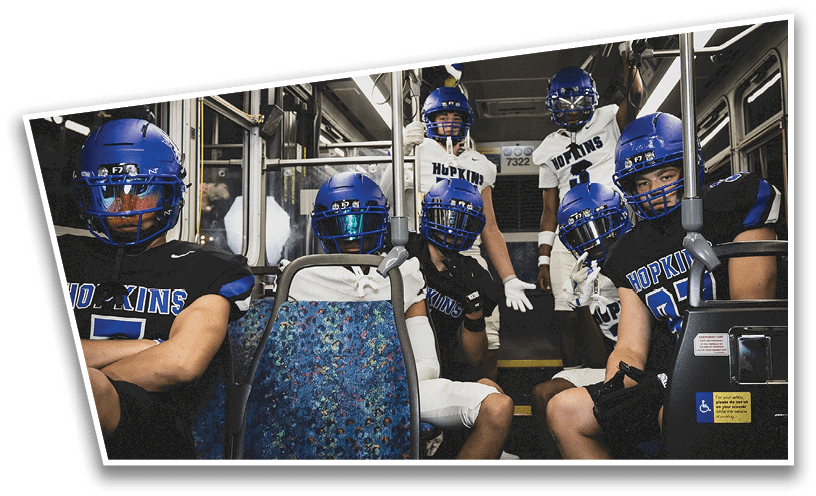 People wearing black American Canyon football uniforms and helmets are standing on a football field at night. Description generated by AI