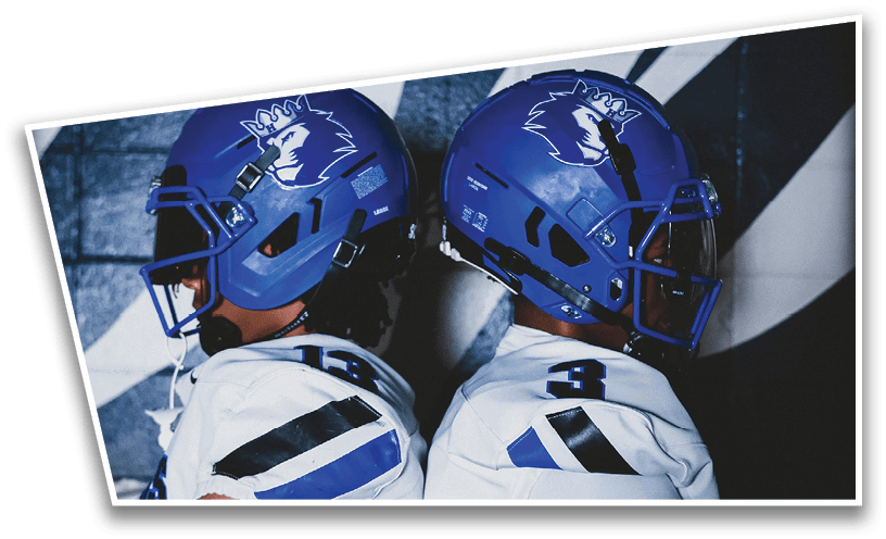 People wearing black American Canyon football uniforms and helmets are standing on a football field at night. Description generated by AI