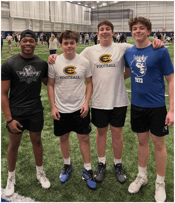 Three football players in blue and white uniforms running on a field. Description generated by AI