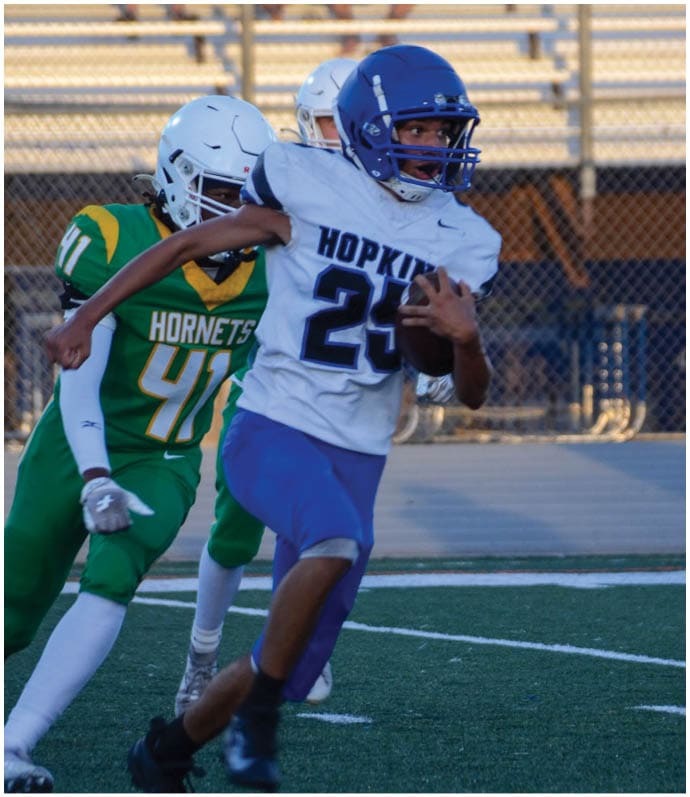Three football players in blue and white uniforms running on a field. Description generated by AI
