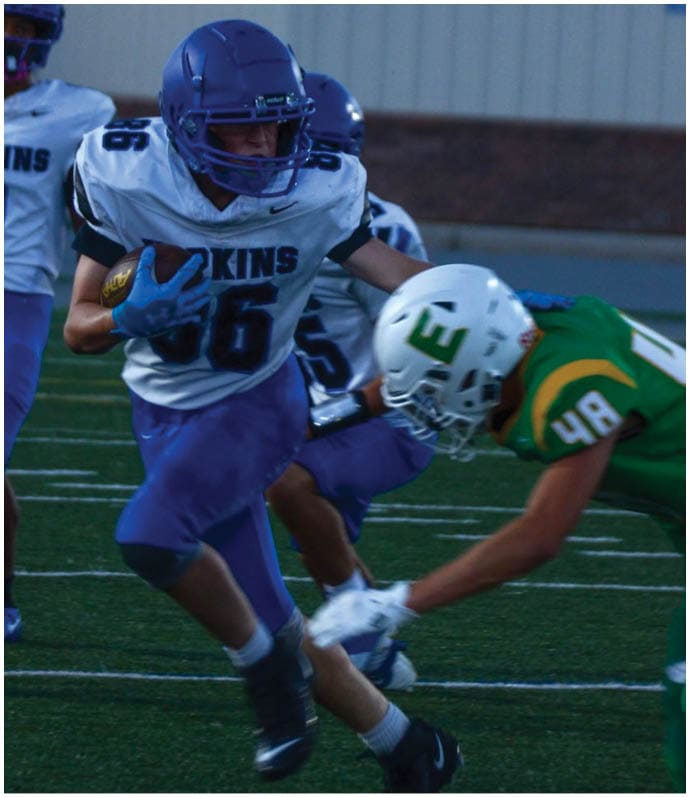 Three football players in blue and white uniforms running on a field. Description generated by AI
