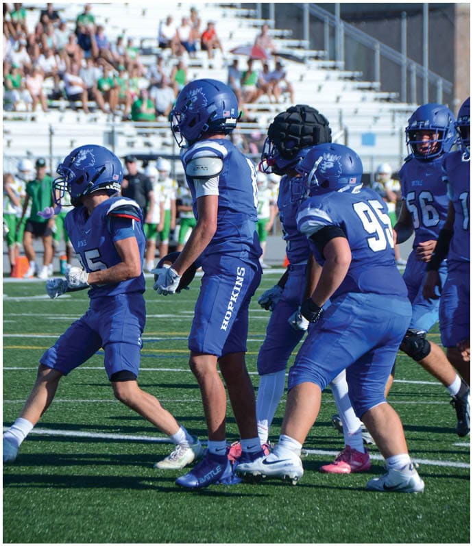 Three football players in blue and white uniforms running on a field. Description generated by AI