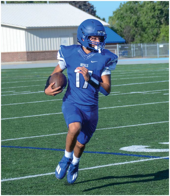 Three football players in blue and white uniforms running on a field. Description generated by AI