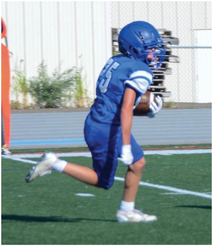 Three football players in blue and white uniforms running on a field. Description generated by AI