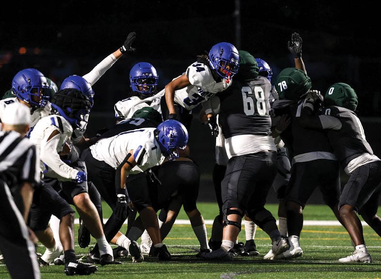Four people wearing black football uniforms with “VISTA" on the front are standing together in a stadium with a crowd in the background, two of them holding helmets raised above their heads. Description generated by AI