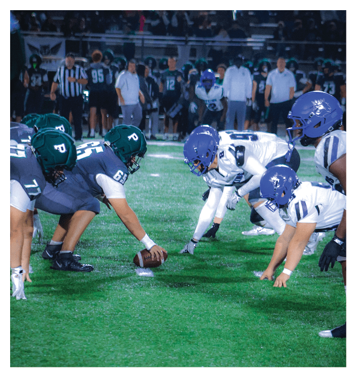 A football game is in progress with players on the field. One player is throwing a football while another player is trying to catch it. The players are wearing uniforms and are actively engaged in the game. AI generated content