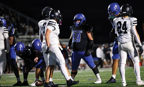 Two men wearing football uniforms are hugging each other on a field. AI generated content